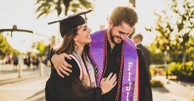 Two recent graduates in caps and gowns laugh and celebrate