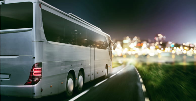 a charter bus drives into a large, lit-up city at night