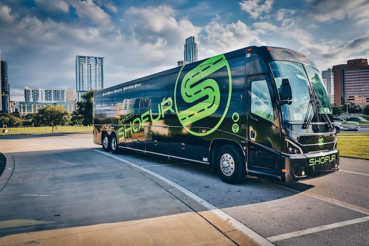 a black bus with the green "shofur" logo parked in a parallel parking spot