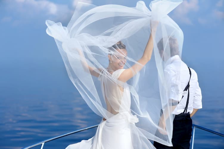 Bride and groom on boat covered by blowing veil