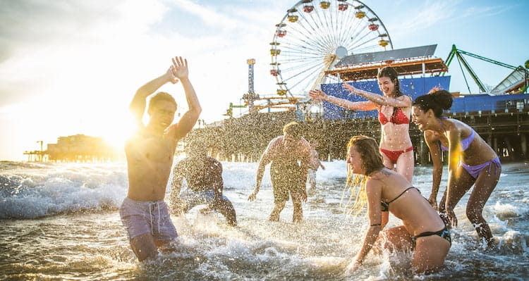 a group of friends splash in the ocean near a boardwalk amusement park