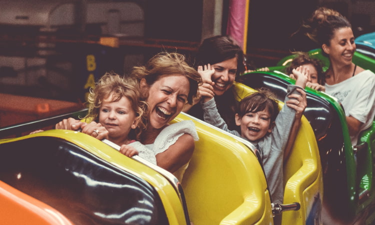 a large family yells and cheers as they ride a roller coaster in a theme park