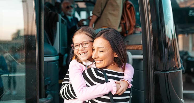 A mother and child embrace at the entrance of a charter bus rental