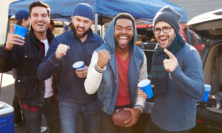 A group of sports fans cheer and celebrate at a football tailgate