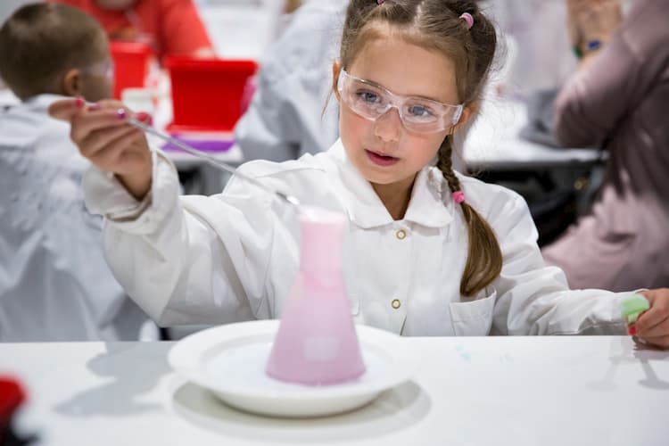 a young girl wearing protective glasses performs a science experiment with a chemical reaction