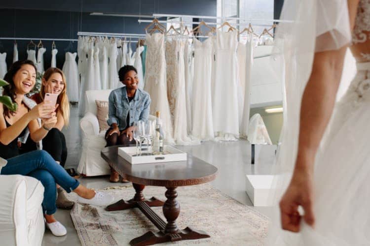 A woman showing her friends a wedding dress that she is trying on and they are smiling.